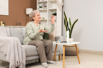 Senior woman with pills sitting on sofa at home