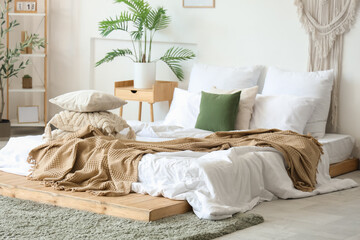 Cozy bed with soft pillows and crumpled blanket in interior of light bedroom