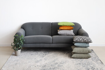 Grey sofa with stacks of pillows near white wall