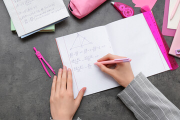 Woman writing math formulas in copybook and stationery on grunge background