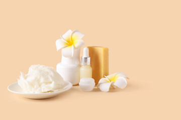Plate of shea butter with bottle of cosmetic oil, soap bar and plumeria flowers on beige background