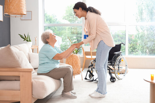 Young African-American female medical worker helping elderly woman in nursing home
