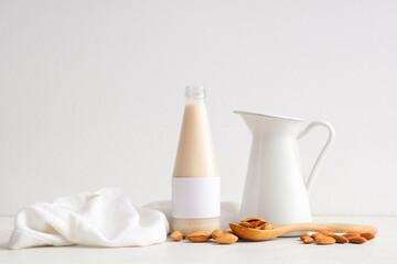 Bottle and jug of fresh almond milk with nuts on white background