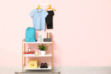 Rack with stationery, decor and stylish school uniform hanging on pink wall