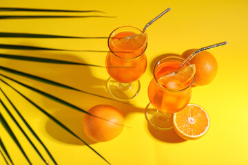 Glasses of Aperol spritz cocktail and palm leaf on yellow background