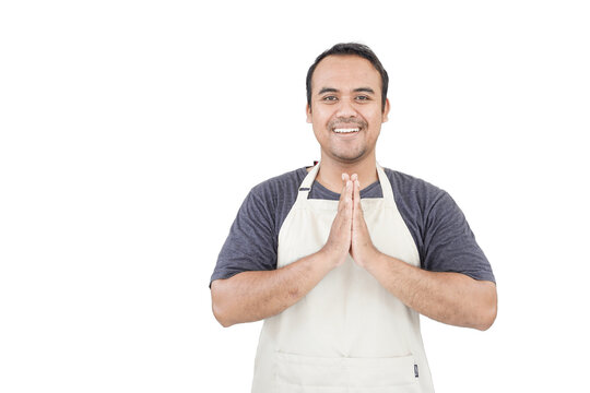 Young smiling Asian man as grocery store staff standing at cashier counter with arms namaste pose and full of confidence in front of display shelves