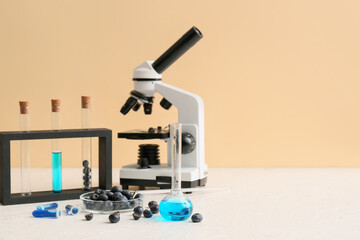 Professional laboratory glassware with microscope and blueberries in Petri dish on table near yellow wall