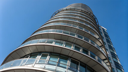 A tall building featuring a sleek, curved glass facade reflecting the sky and surrounding environment
