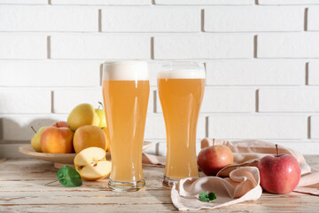 Glasses of fresh apple kvass and plate with fruits on white wooden table
