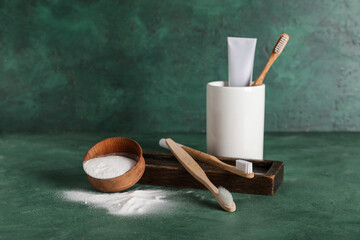 Bowl of tooth powder with brushes, holder and toothpaste on table against green grunge background