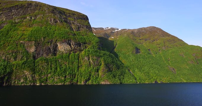 Majestic green cliffs and deep blue fjord waters under cloudy skies, filmed from a cruise ship sailing through the breathtaking landscapes of Norway fjords.