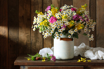 still life with garden flowers daisies and Turkish carnations in a milk can on a dark wooden background