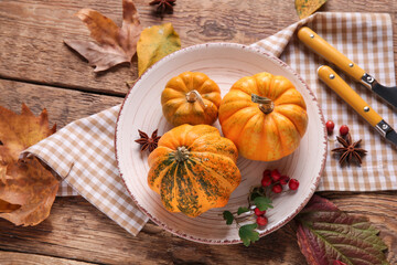 Plate with fresh pumpkins, star anise, rose hip berries and autumn leaves on wooden background