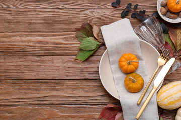 Autumn table setting with pumpkins and fallen leaves on wooden background