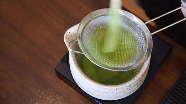Matcha tea brewing Japanese style with fine mesh strainer over ceramic bowl and pot creating smooth calm traditional tea preparation experience