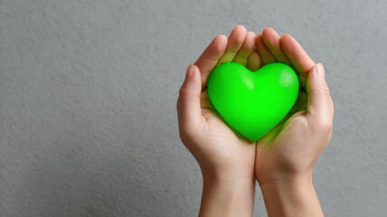 Fototapeta premium Two hands delicately cupping a vibrant green heart, conveying feelings of love, care, and compassion