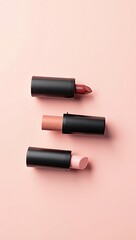 Obraz premium Minimalist flat-lay of three lipstick tubes in matte black casing arranged diagonally on pastel pink background with soft shadows. 
