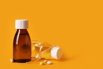 Bottles of cough syrup with measuring spoon and pills on orange background