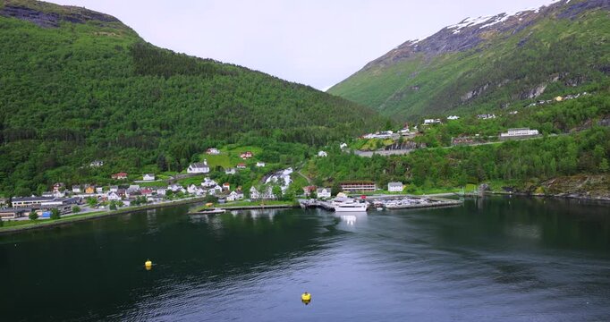 View on Hellesylt, a small village in the Sunnylvsfjord, Norway. Captured from a large cruise ship, the scene features a lush green landscape, a waterfall, and serene fjord waters.