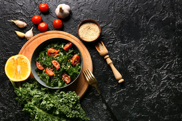Composition with bowl of tasty kale salad and different ingredients on dark background