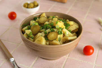 Bowl of tasty potato salad with green onion and pickled cucumber on pink tile background