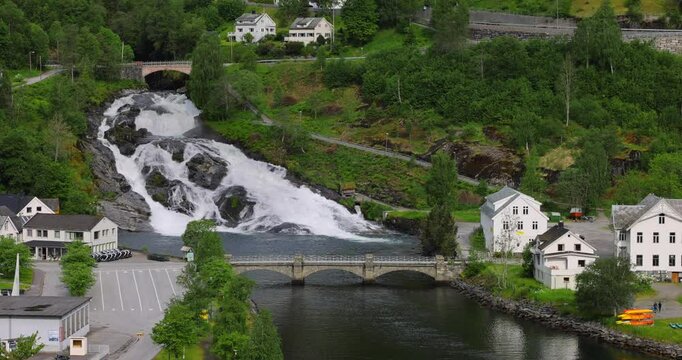 View on Hellesylt, a small village in the Sunnylvsfjord, Norway. Captured from a large cruise ship, the scene features a lush green landscape, a waterfall, and serene fjord waters.