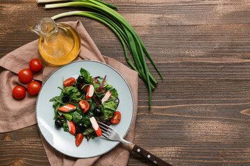 Plate of salad with crab sticks, spinach, black olives and tomatoes on wooden background