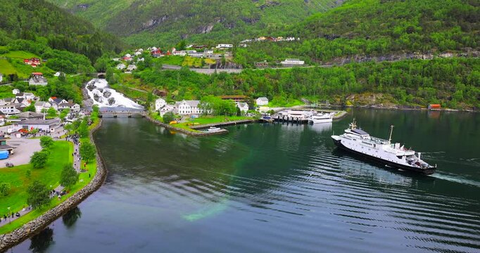 View on Hellesylt, a small village in the Sunnylvsfjord, Norway. Captured from a large cruise ship, the scene features a lush green landscape, a waterfall, and serene fjord waters.