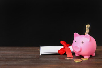 Piggy bank with money and diploma on table near blackboard. Student loan concept