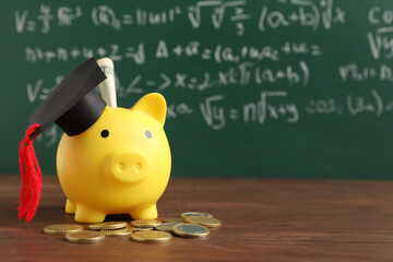 Piggy bank with graduation hat and money on table near green blackboard. Student loan concept