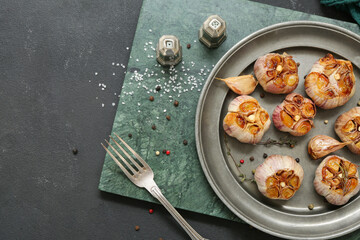 Plate with baked garlic, peppercorns and thyme on black background
