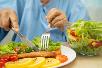 Asian elderly woman patient eating salmon stake and vegetable salad for healthy food in hospital.
