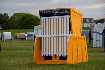 Traditional German wicker beach chair (Strandkorb) standing on green grass, closed and striped canopy up, symbolizing leisure, summer, and classic European outdoor design.