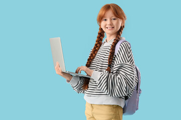 Cute ginger girl with backpack and modern laptop on blue background