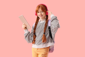 Cute ginger girl with modern tablet computer and headphones on pink background