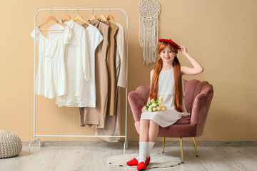 Cute ginger girl in stylish dress with beautiful flowers sitting on armchair in hall