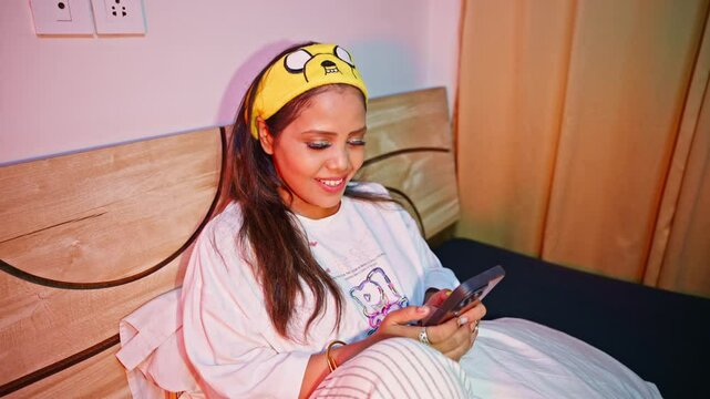 Lady sitting on bed with headband scrolling her mobile