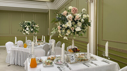 Elegant dining setup in a banquet hall with white tables, floral arrangements, and colorful fruit platters. Numbered tables 5 and 6 with glasses and appetizers, perfect for special events