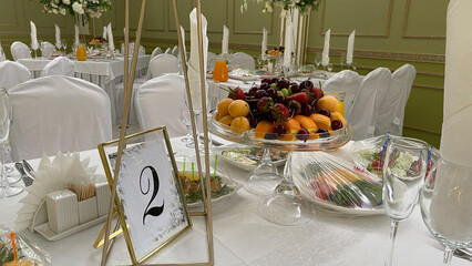 Elegantly arranged dining table for a celebration event, featuring a fruit platter, fresh salads,...