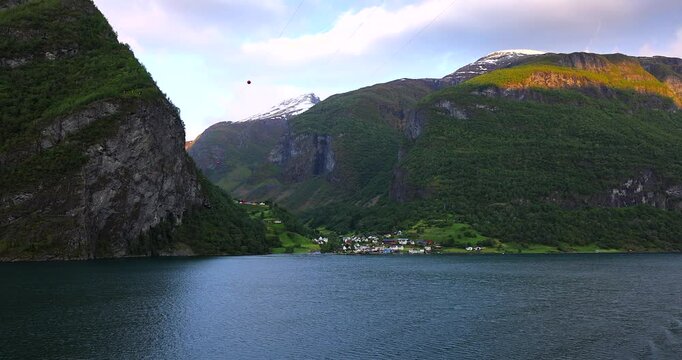 Majestic green cliffs and deep blue fjord waters under cloudy skies, filmed from a cruise ship sailing through the breathtaking landscapes of Norway fjords.