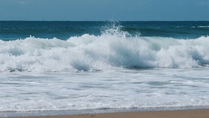 Waves crashing onto a sandy beach under a clear blue sky