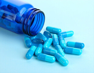 Blue capsules spilling from a dark blue plastic bottle onto a light blue background.
