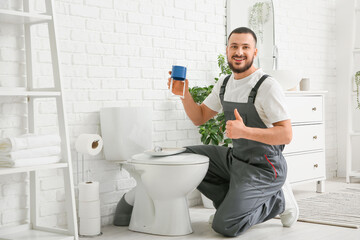 Male plumber with toilet fill valve showing thumb-up in restroom
