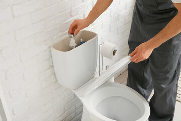 Male plumber repairing toilet tank in light restroom, closeup