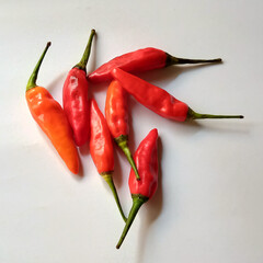 Fresh red bird's eye chilies naturally spread on a pure white background, highlighting their vivid...