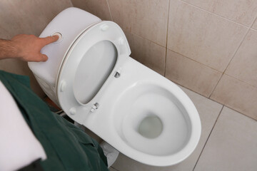 Male plumber flushing fixed toilet in restroom, top view