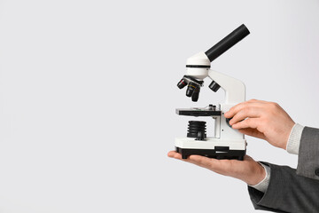 Male teacher holding microscope on grey background, closeup