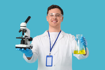 Young male scientist with microscope and chemical flask on blue background