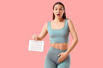 Shocked sporty young woman with menstrual calendar on pink background