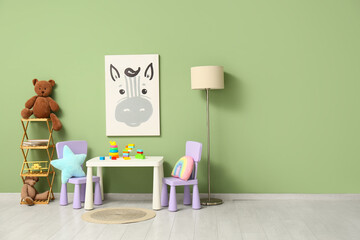 Interior of children's room with lamp, play table and many toys in shelving unit near green wall